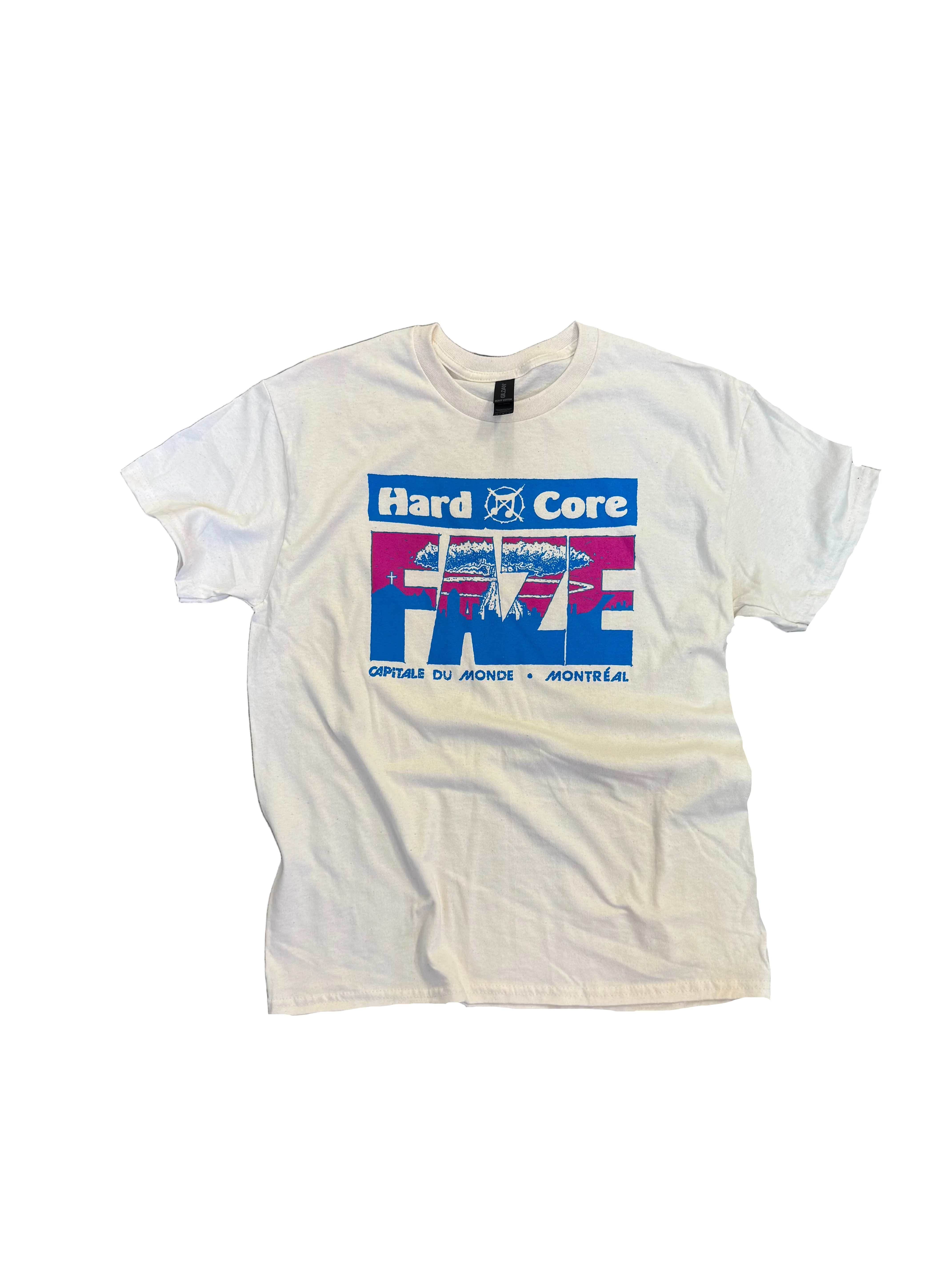 A white short-sleeve graphic T-shirt laid flat on a weathered concrete floor. The shirt features a large front graphic with the words 'Hard Core' and 'FRÉ' in red, white, and blue, with a mountain illustration.