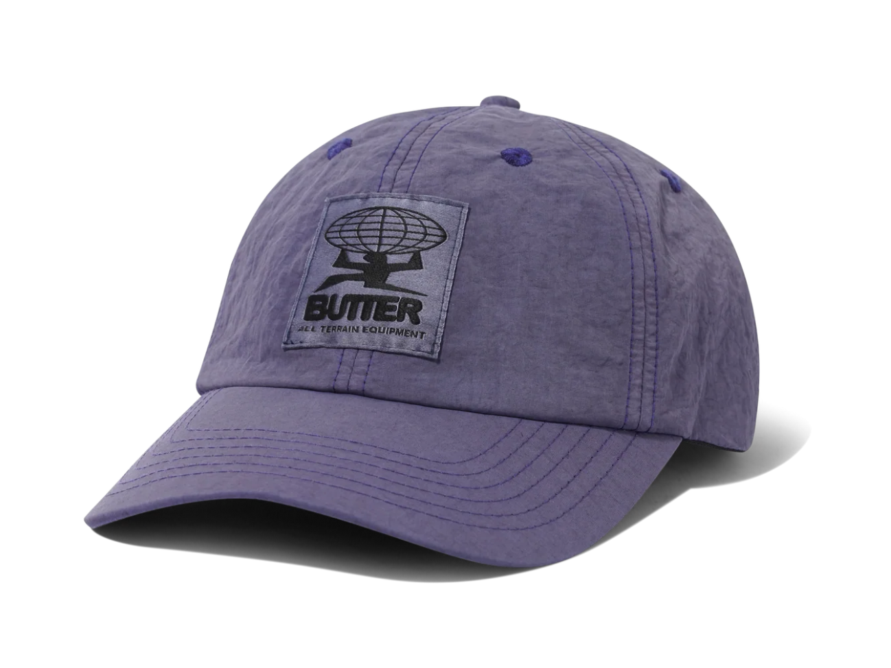 A purple cotton baseball cap with a black embroidered patch on the front that reads 'BUTTER' and 'A TERMINAL EQUIPMENT' with a globe logo. The cap is photographed on a clean white background with a soft shadow.