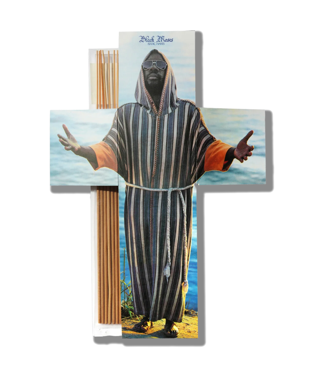 A cross-shaped wall art piece featuring a printed photo of a hooded figure with outstretched arms over a beach scene, with a bundle of wooden dowels or rods attached along the left side. The text 'Rich Man' appears at the top.