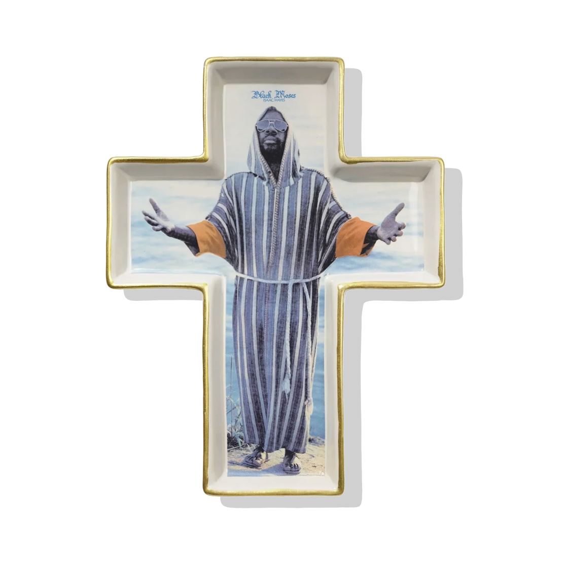 A white ceramic cross-shaped tray with gold trim, featuring a printed image of a hooded figure in a striped robe standing on a beach, photographed against a plain white background.